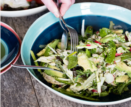 Hand tossing a fresh green salad in a large Musango bowl in layered shades of blue
