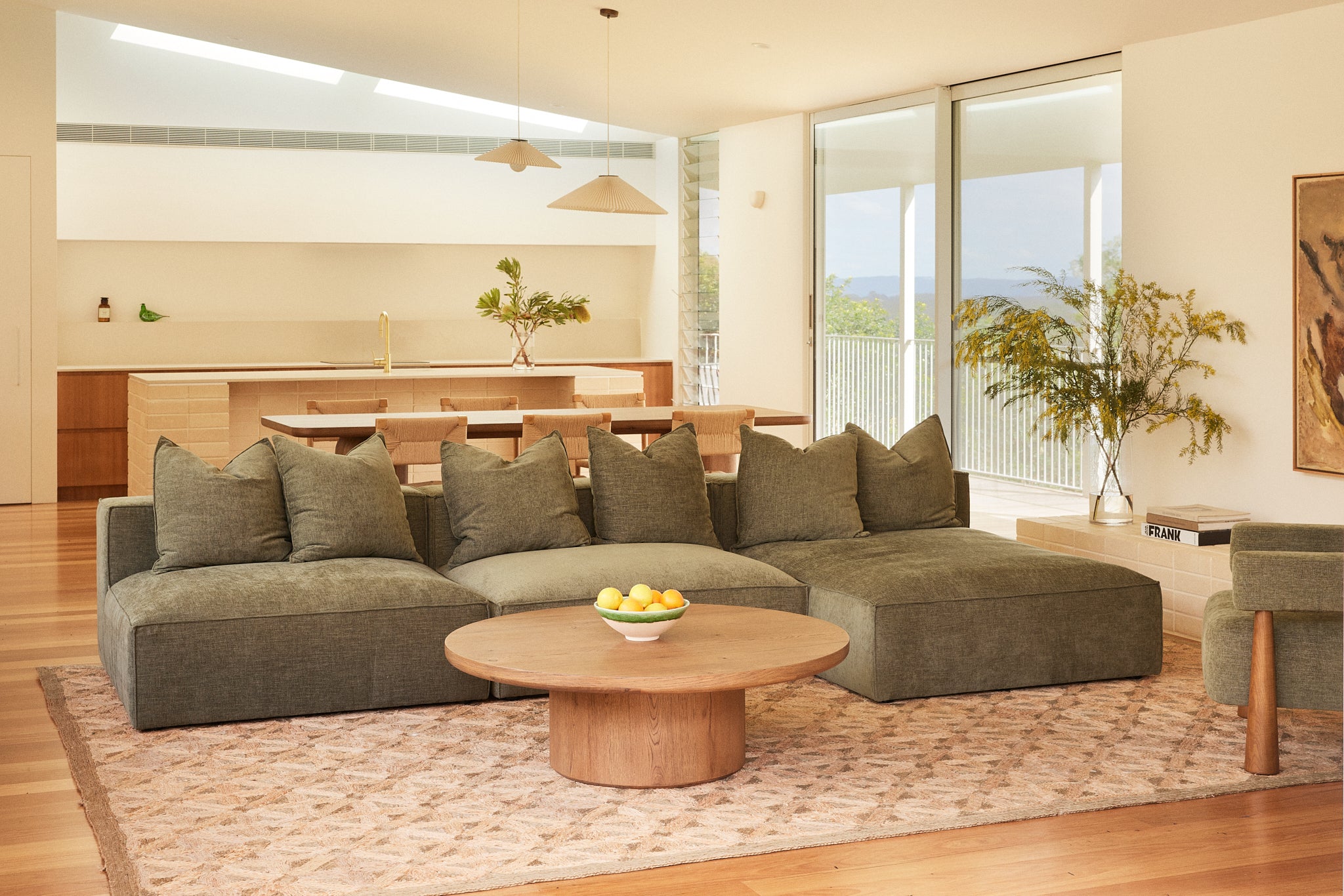 Cosmos modular sofa with chaise in Forest fabric styled with the Alta round coffee table in aged brown Oak in a contemporary Australian living room with an open-plan kitchen.