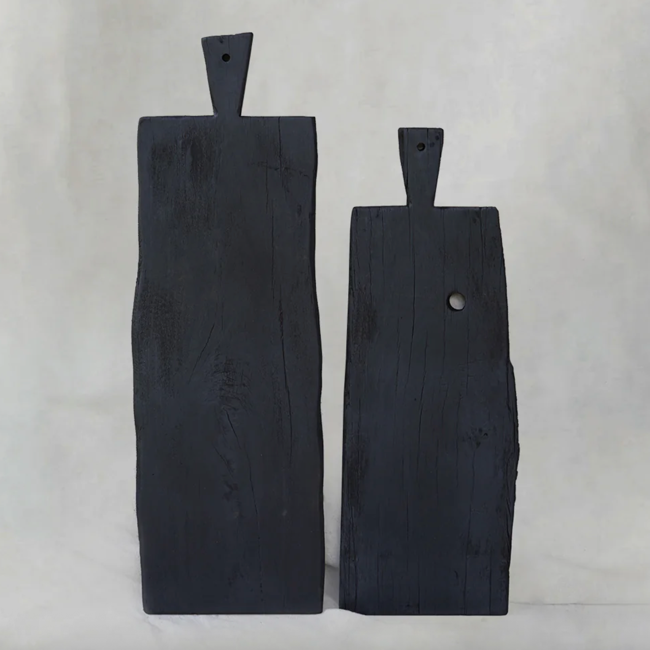 Two handcrafted black hardwood chopping boards from Moku Collective, featuring organic edges and carved handles, displayed upright