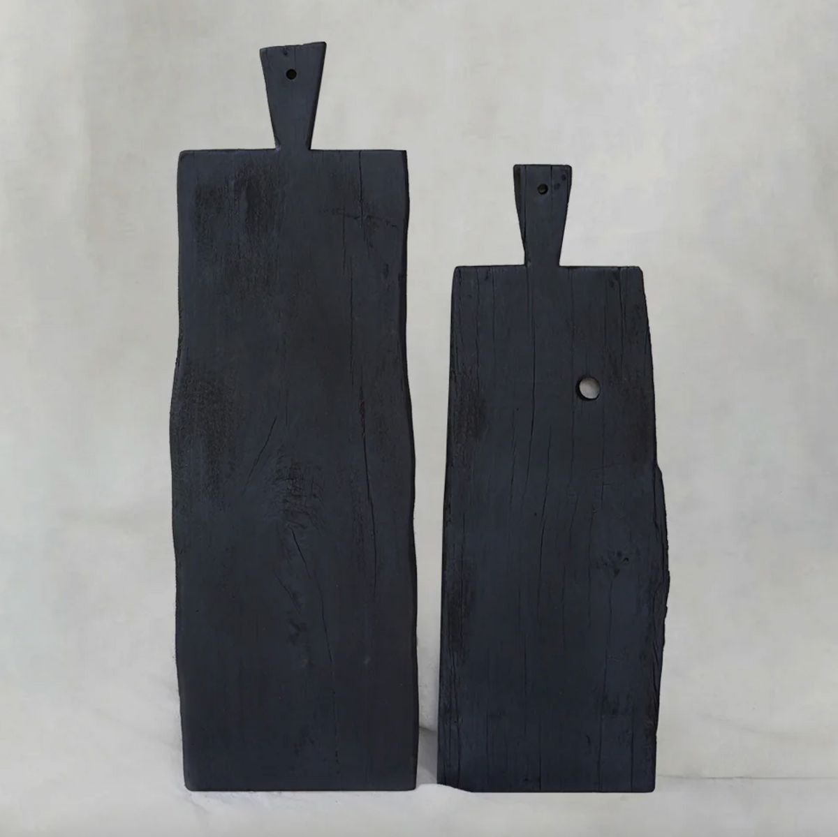Two handcrafted black hardwood chopping boards from Moku Collective, featuring organic edges and carved handles, displayed upright