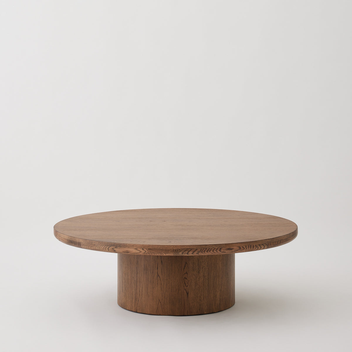 Round oak coffee table with pedestal base in aged Brown finish.
