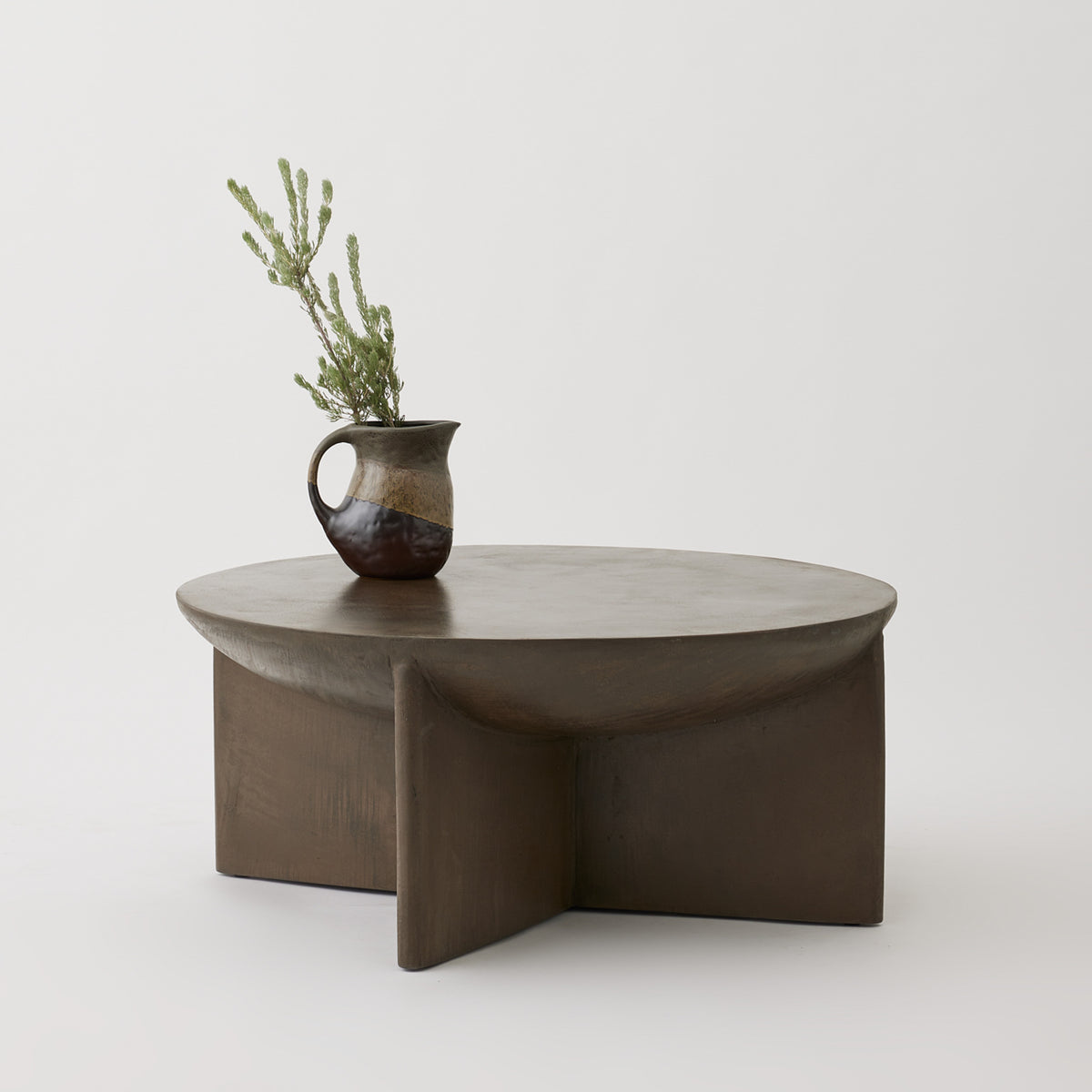 Axel round coffee table in Pebble micro-cement with sculptural base, styled with ceramic vase