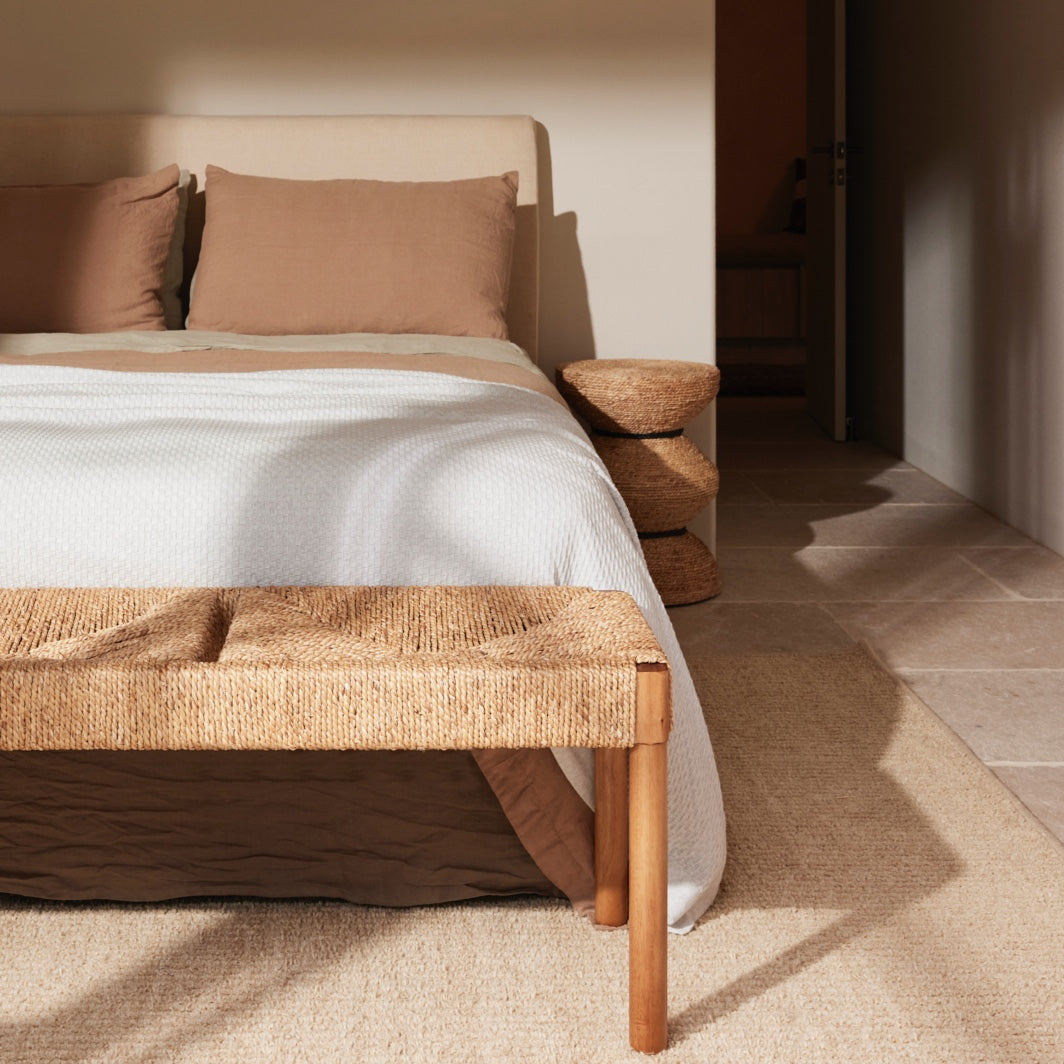 Tiki side table in woven banana leaf rope, styled in a modern bedroom.