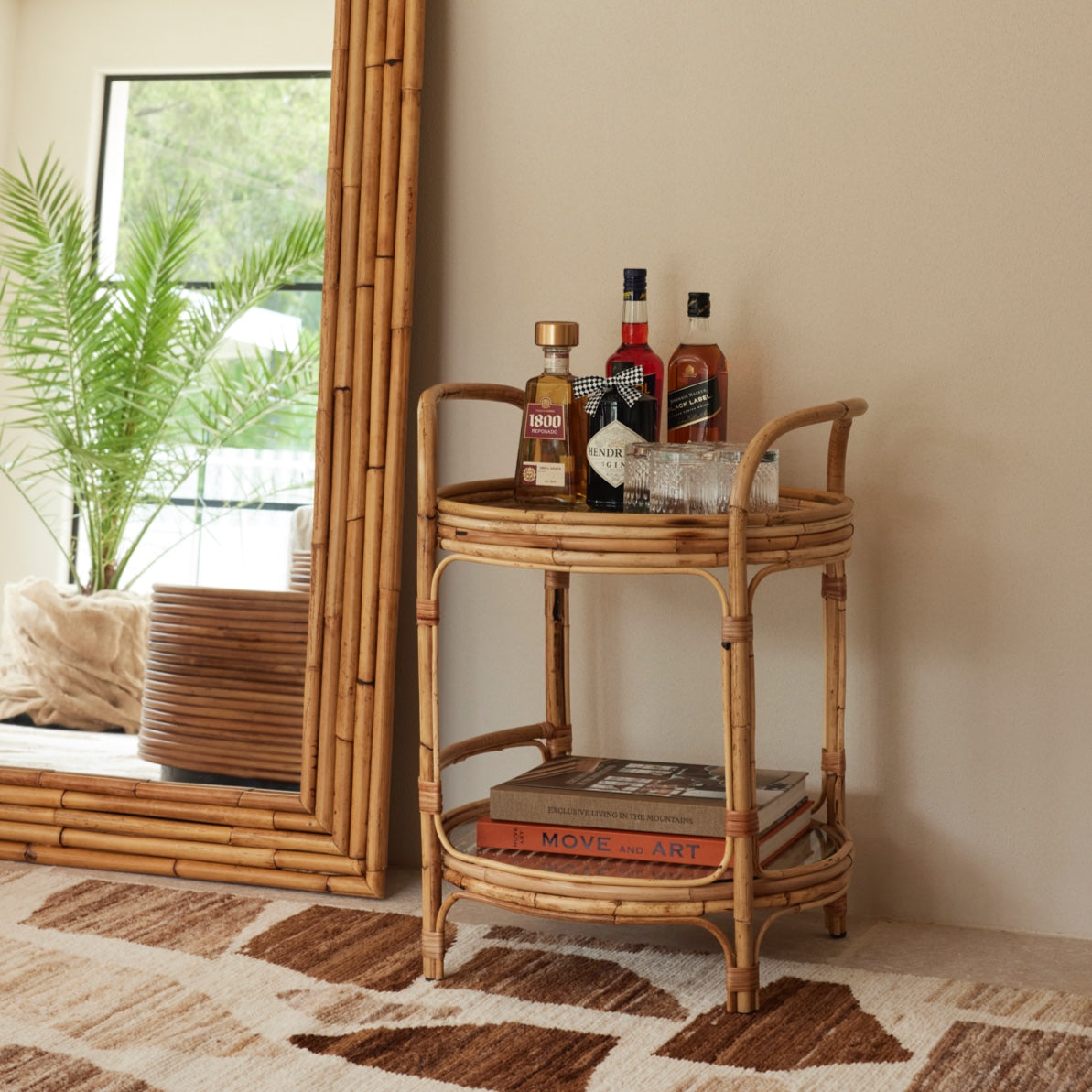 Capri bar trolley styled with bottles and glassware, handcrafted rattan with two glass shelves.