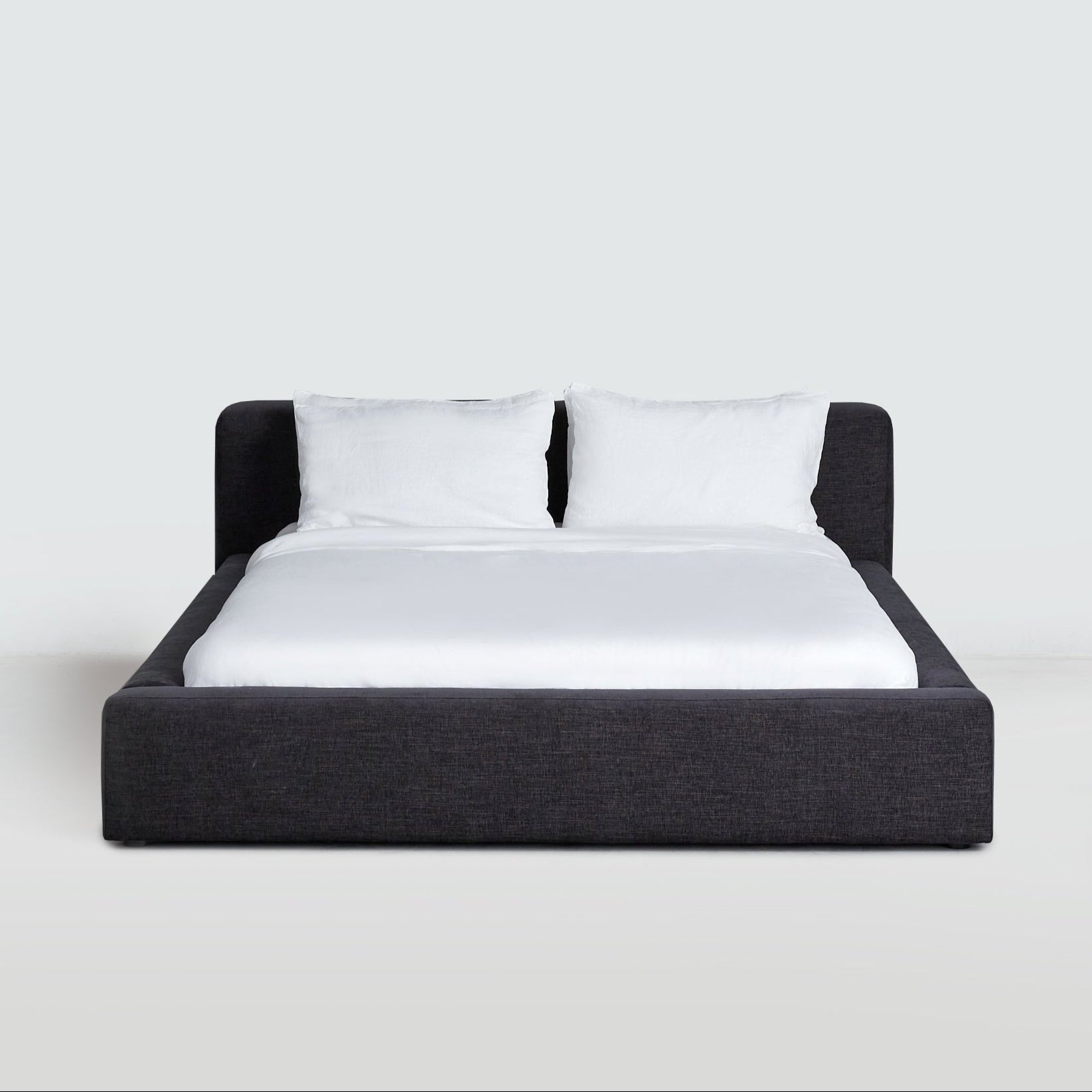 Low-profile upholstered Cosmos Bed in Charcoal, front view, showing wrapped platform frame and cushioned headboard.