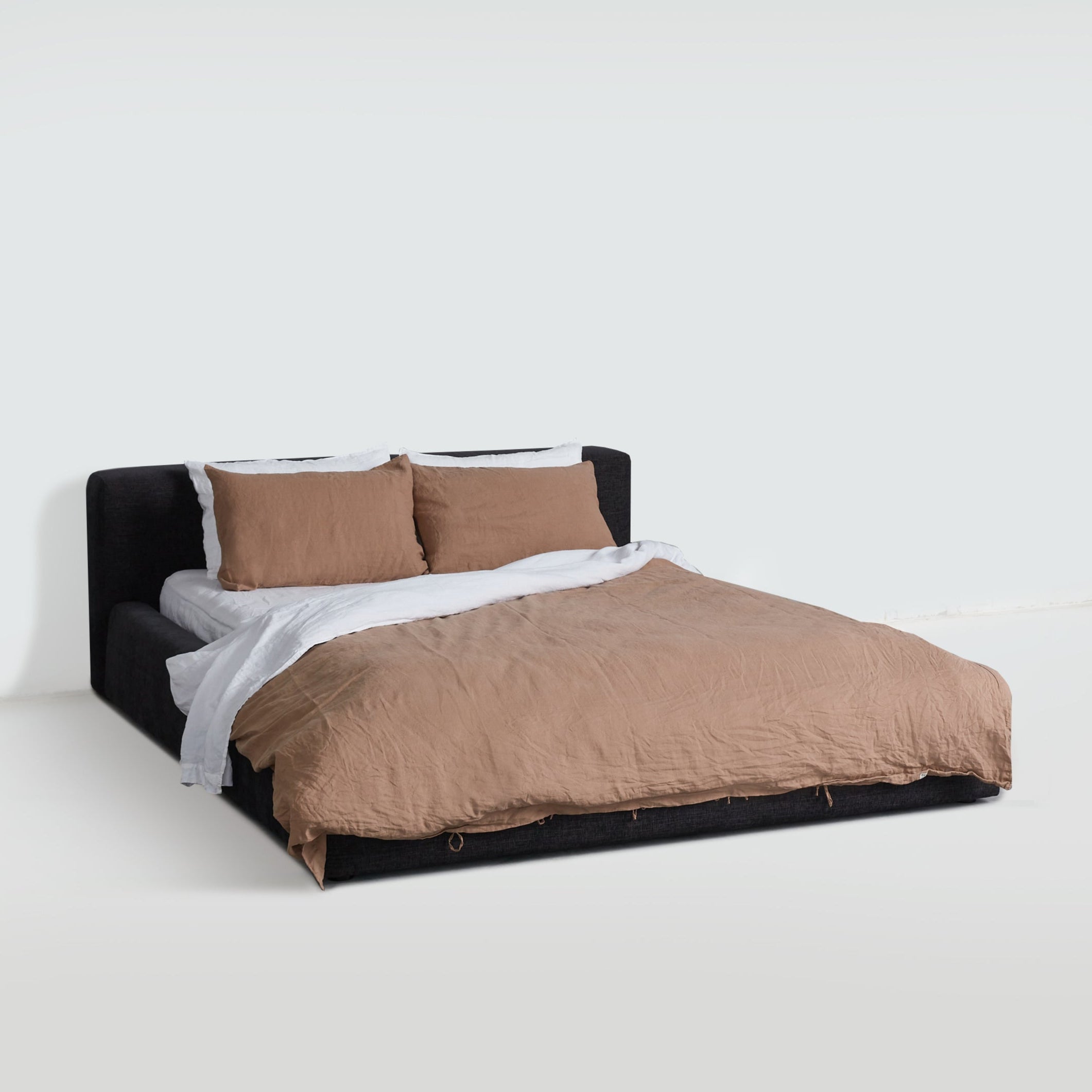 Charcoal Cosmos Bed styled with warm neutral bedding, showcasing soft upholstered frame and low silhouette.