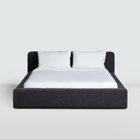 Low-profile upholstered Cosmos Bed in Charcoal, front view, showing wrapped platform frame and cushioned headboard.