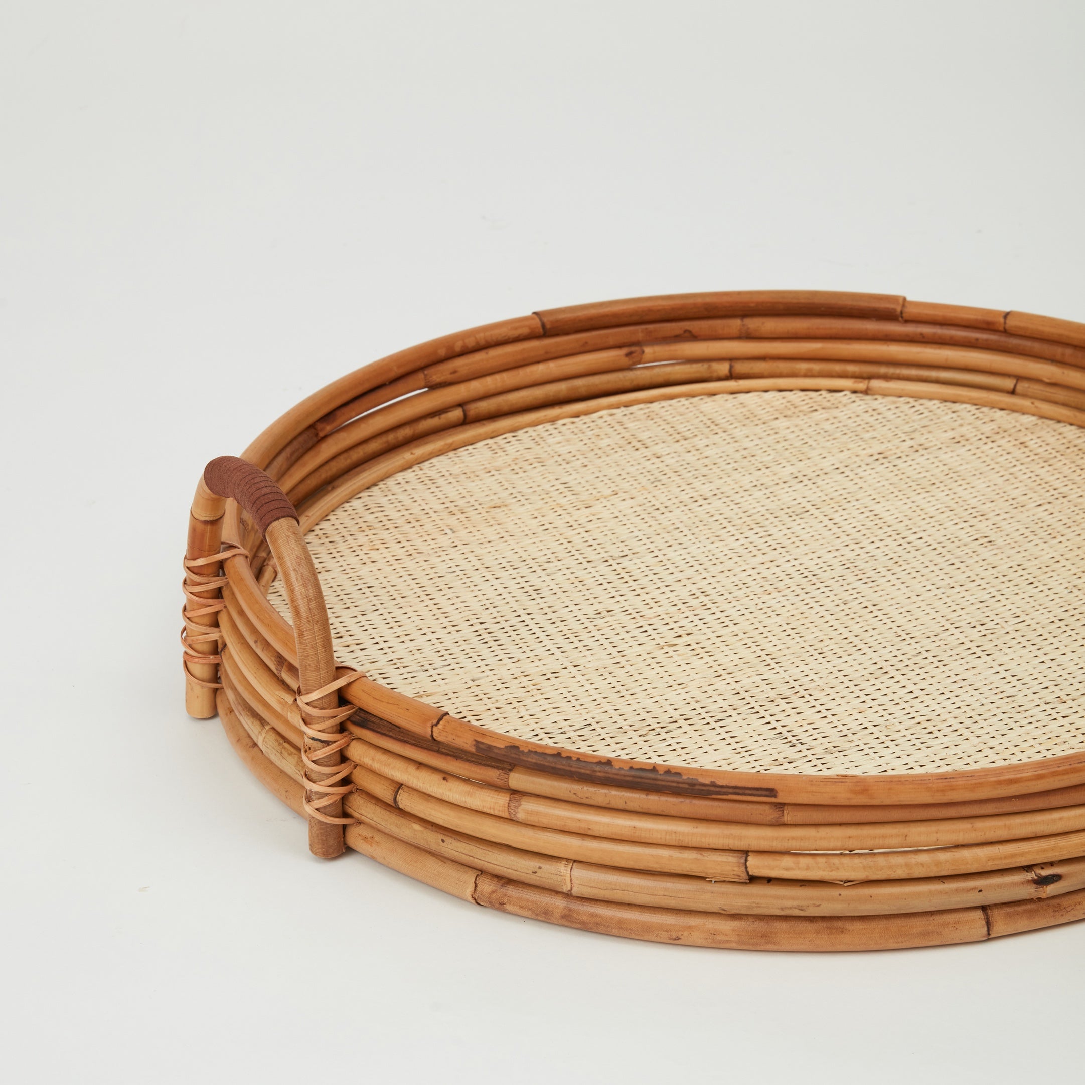 Round Cuba tray handcrafted in natural rattan with raised edges, side view.