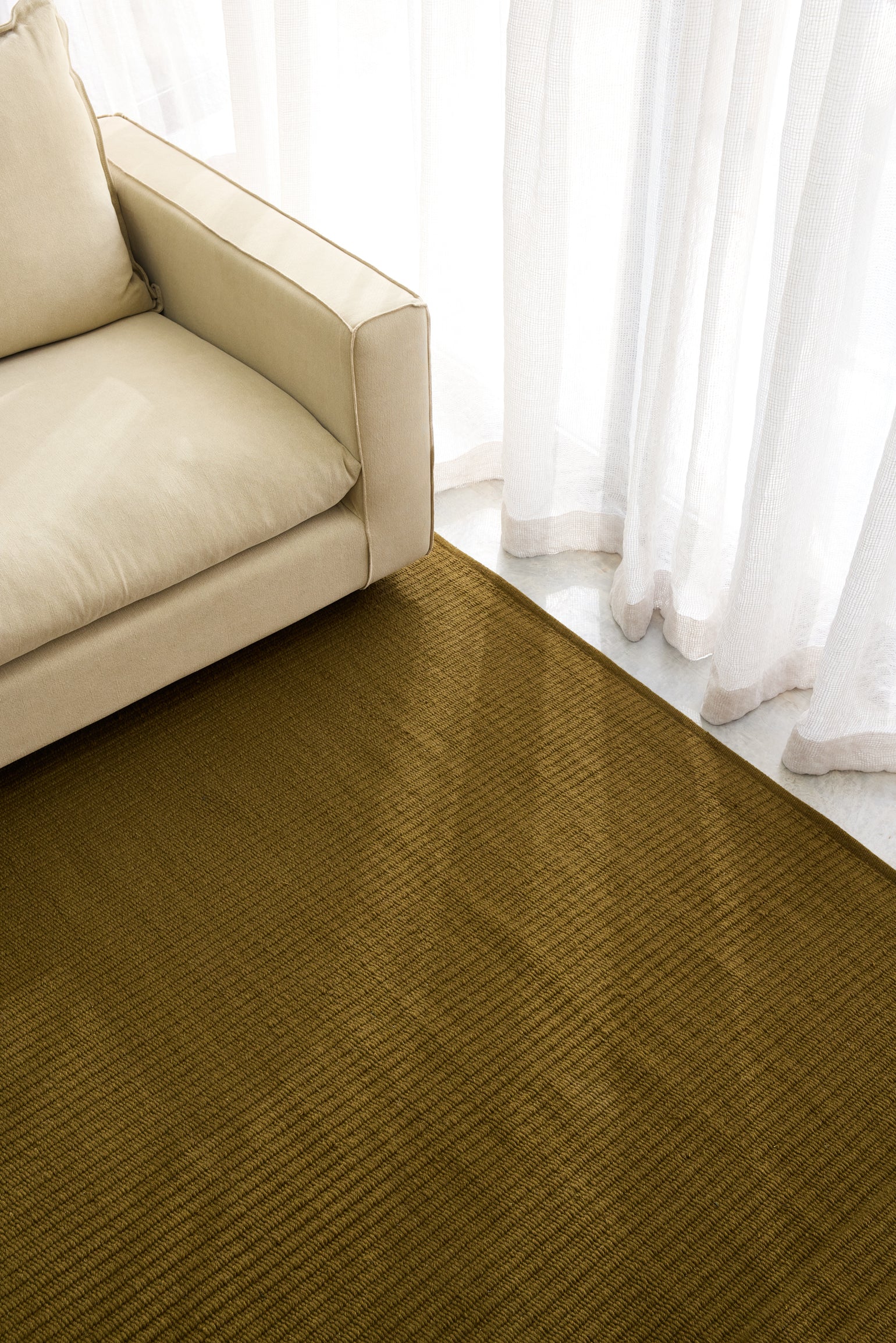 Pebble Flatweave Rug in Khaki – handwoven New Zealand wool under a sofa