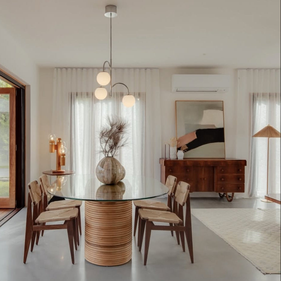 Dining room with the Laguna oval rattan and glass table and wooden chairs, featuring a modern light fixture.