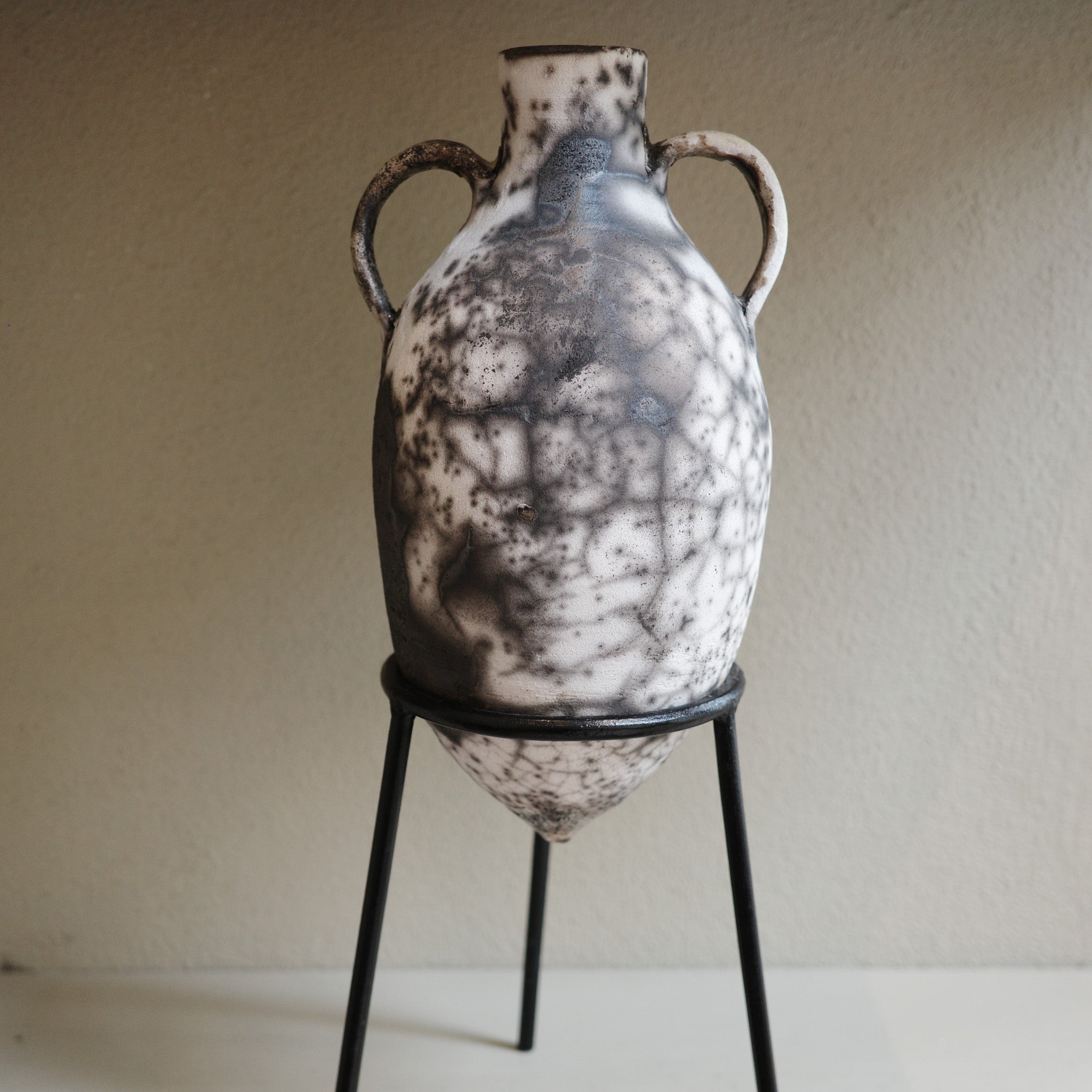 Amphora-style Naked Raku Vase displayed on black metal stand with natural smoky surface